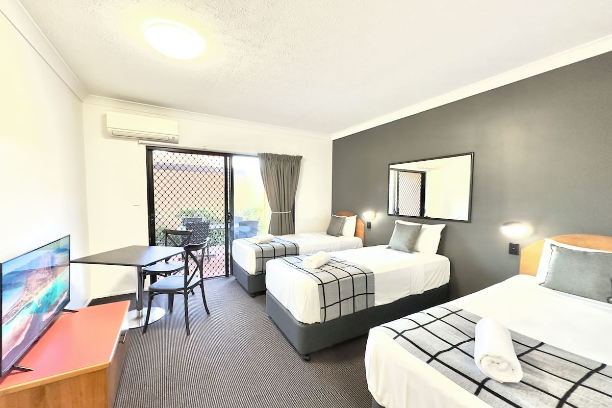 A hotel room with two beds, a desk, a TV, and a balcony with a view.