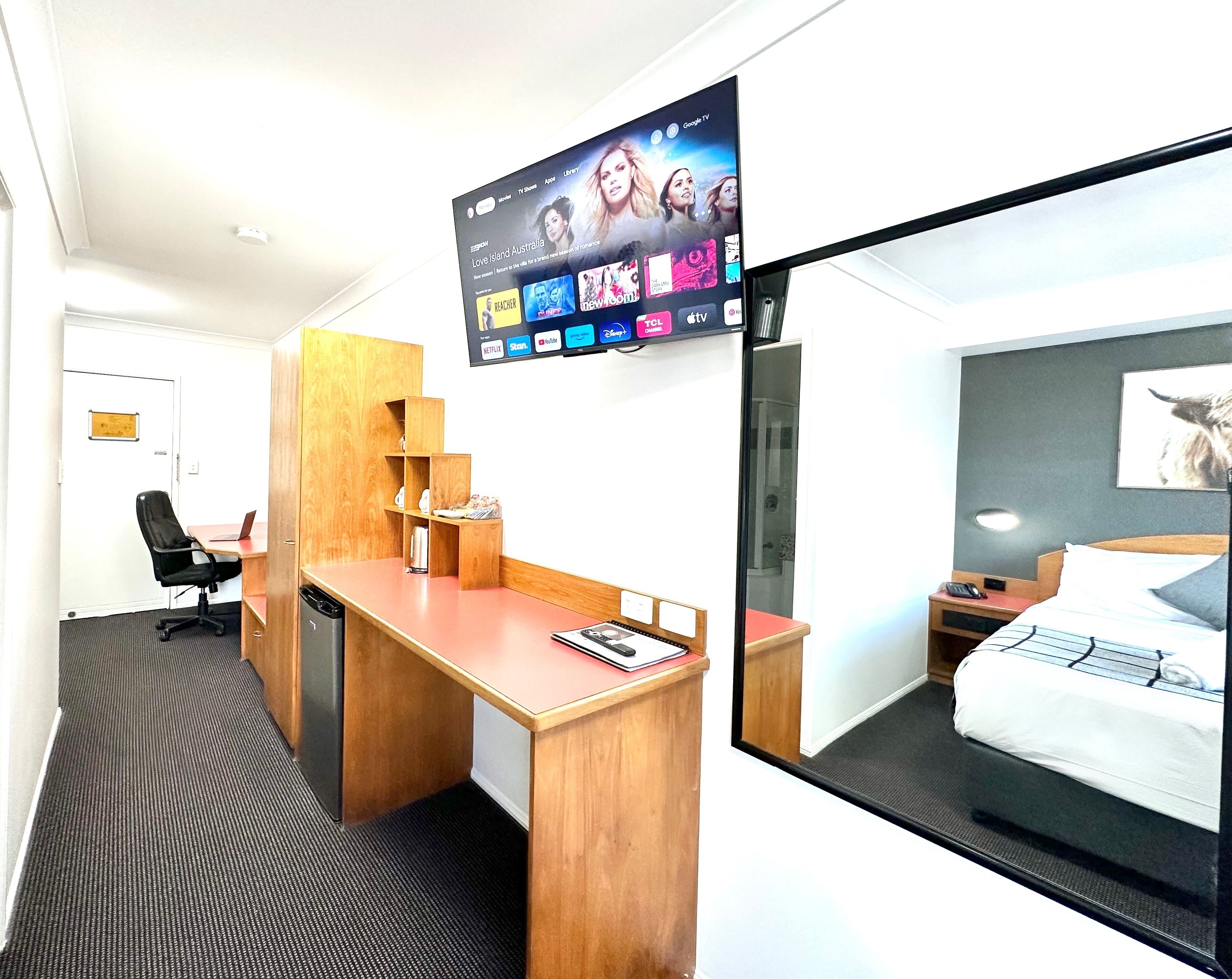 A hotel room with a desk, chair, bed, and a TV mounted on the wall displaying various streaming services.