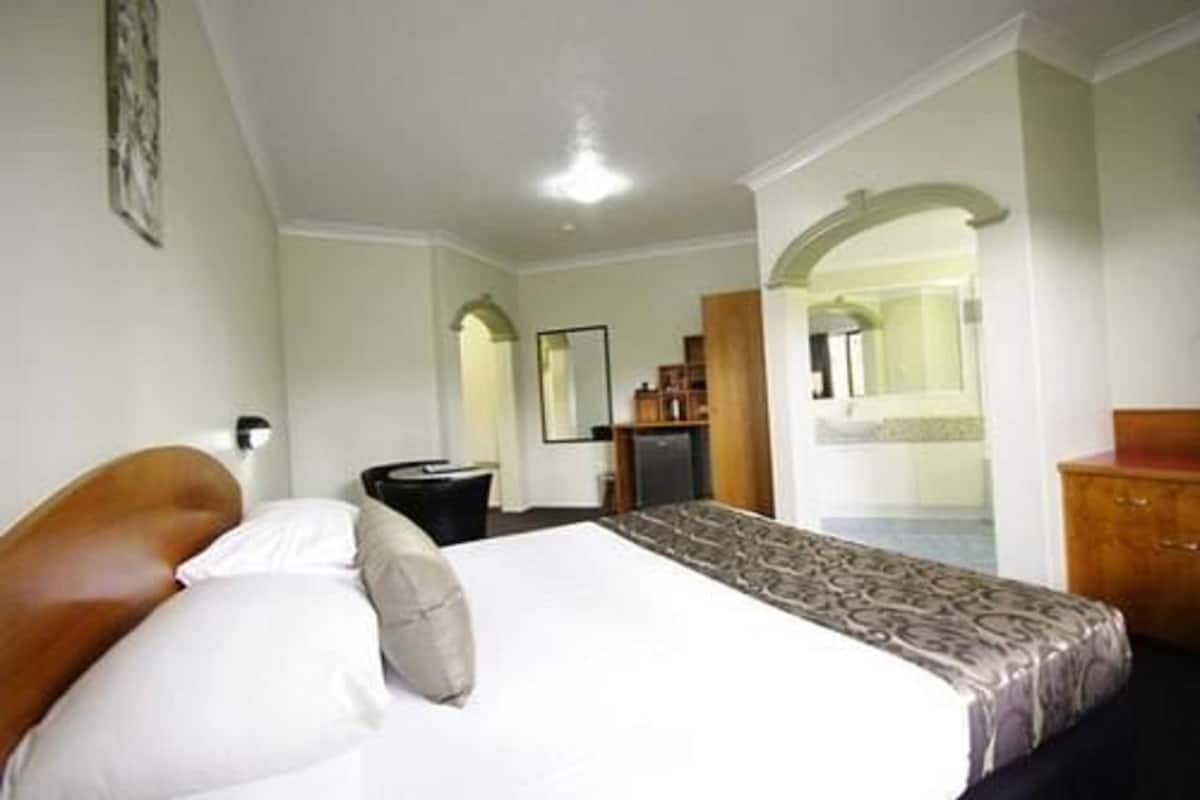 A hotel room with a bed, a desk, a chair, a wardrobe, and a bathroom visible through an archway.