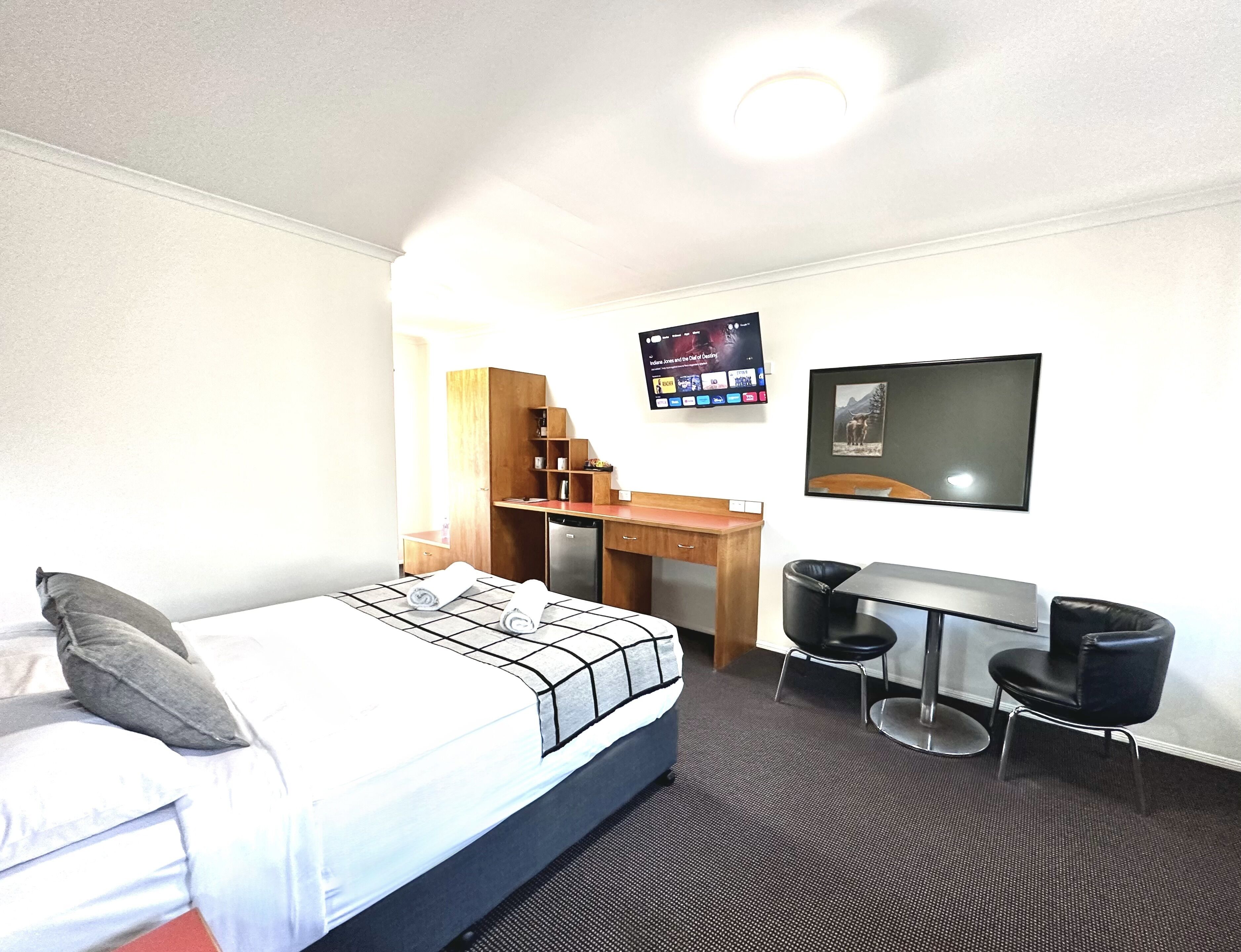 A hotel room with a bed, a desk, a chair, a TV, and a framed picture on the wall.