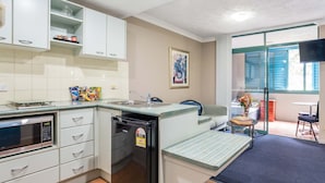 A compact kitchen with white cabinets, a built-in microwave, a refrigerator, and a small dining area with a table and chairs. - Albion Manor (Albion)