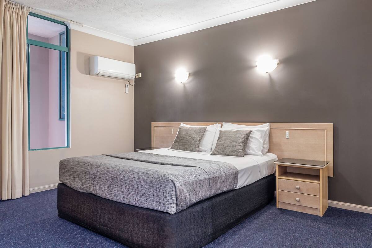 Ein ordentlich eingerichtetes Schlafzimmer mit Bett, Nachttischen und einer Klimaanlage.