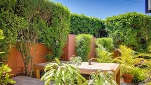 A patio with a wooden table and benches, surrounded by various potted plants and a hedge. - Albion Manor (Albion)