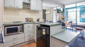 A compact kitchen with white cabinets, a built-in microwave, a black refrigerator, and a small dining area with a table and chairs. - Albion Manor (Albion)