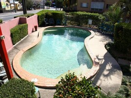 A swimming pool with a curved edge, surrounded by a brick walkway and greenery.