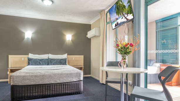 A hotel room with a bed, a TV mounted on the wall, a small table with a chair, and a window with curtains. - Albion Manor (Albion)