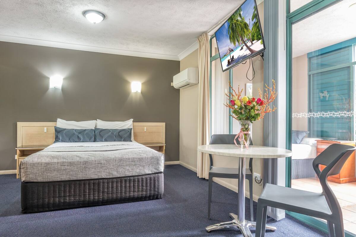 Ein Hotelzimmer mit Bett, Wandfernseher, kleinem Tisch mit Stuhl und einem Fenster mit Vorhängen.