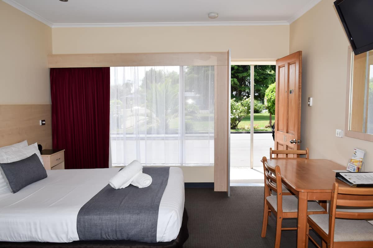 A hotel room with a bed, a desk, and a view of a garden through a sliding door.