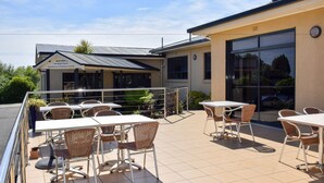 Un patio exterior con mesas y sillas, un edificio con un letrero que dice "Beachway - The Wight Room Functions & Conference Centre", y una puerta de vidrio de acceso.