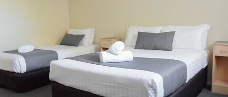 Dos camas individuales con ropa de cama blanca y gris, una mesita de noche pequeña y una mesita auxiliar.
