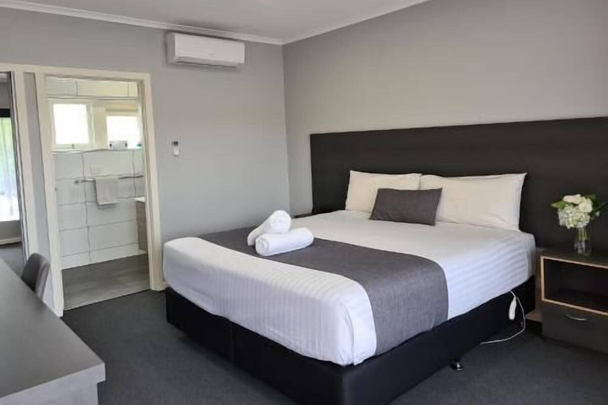 A hotel room with a bed, bedside table, and a bathroom visible through an open door.