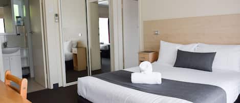 Una habitación de hotel con cama, escritorio, silla, armario y baño.