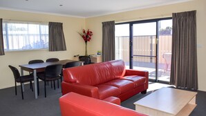 Una habitación con un sofá de cuero rojo, una mesa de comedor con sillas, una pequeña mesa de centro de madera y un ventanal corredizo que da a un espacio exterior.