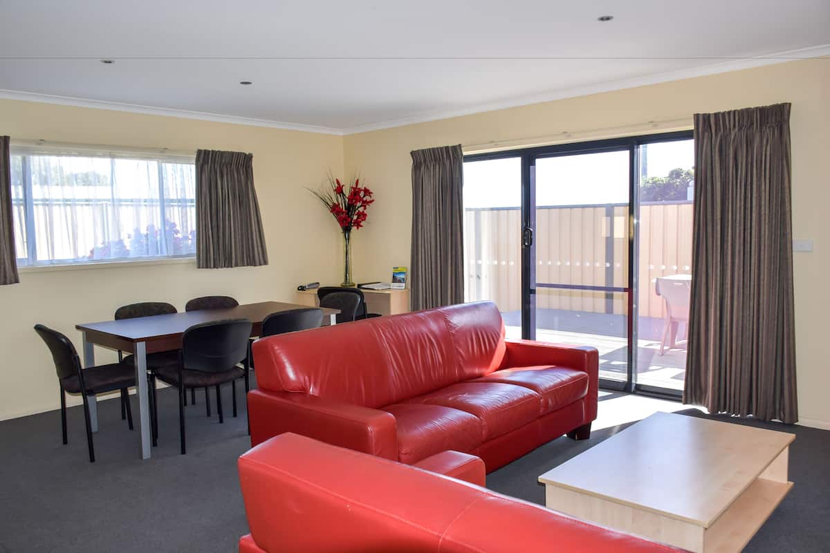 A room with a red leather sofa, a dining table with chairs, a small wooden coffee table, and a sliding glass door leading to an outdoor area.