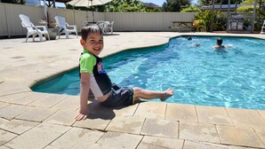 Niño sentado junto a una piscina, con un área de patio al fondo.
