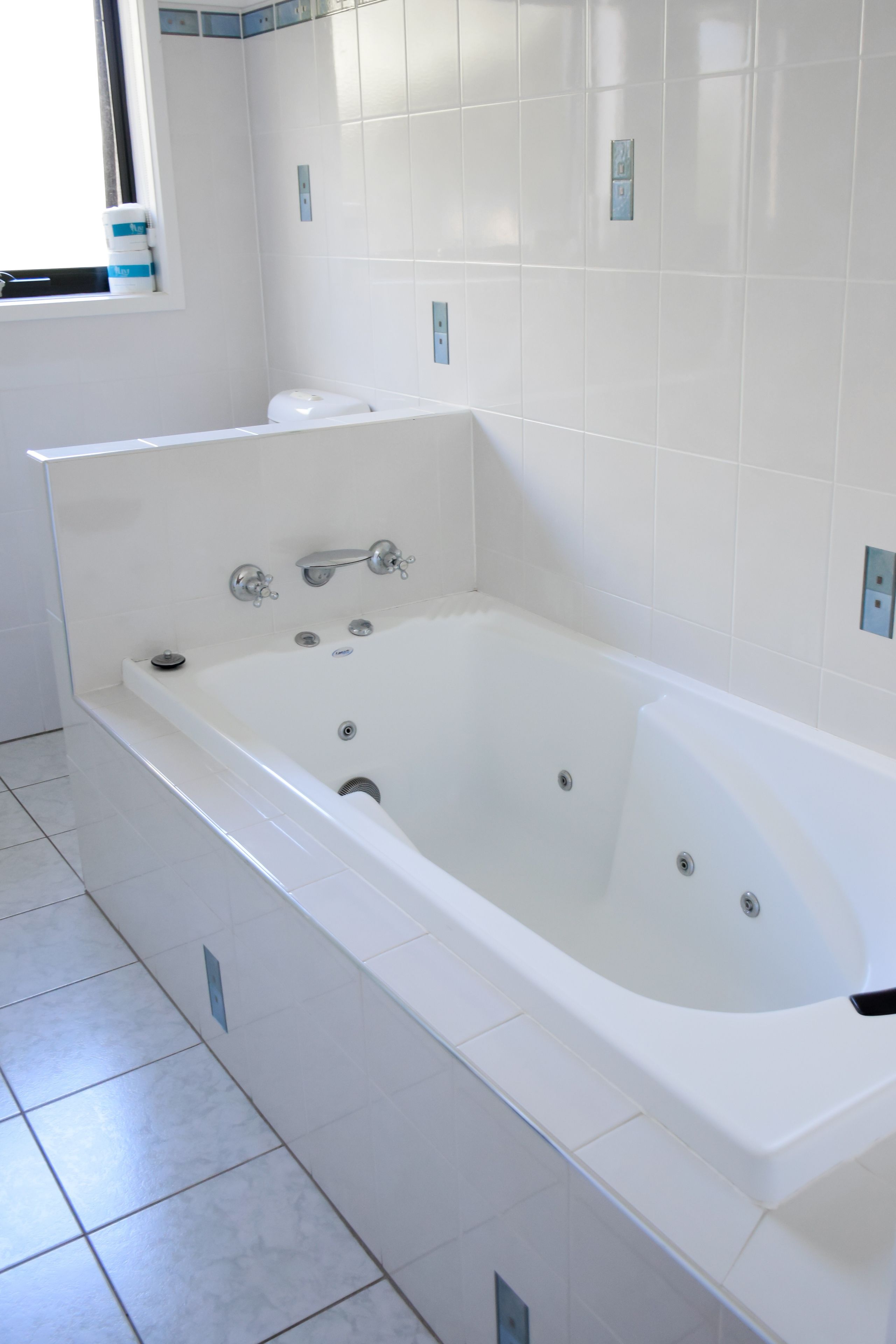 A modern bathroom with a large bathtub, white tiles, and a window with a view.