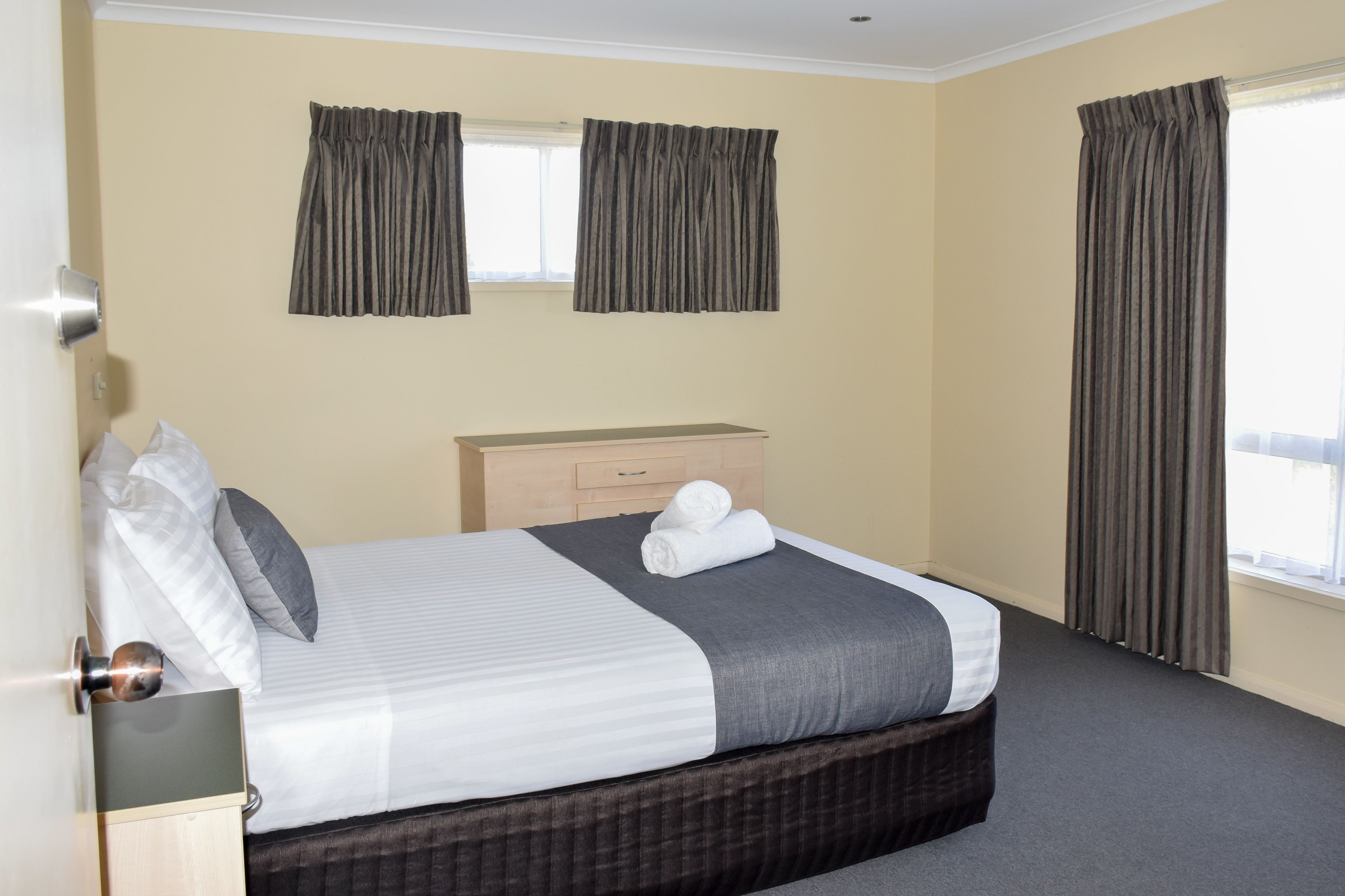 A neatly made bed with a grey and white striped bedspread, a wooden nightstand, and a dresser with a mirror.