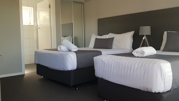 Habitación de hotel con dos camas, un espejo, una lámpara de noche y vista al pasillo.