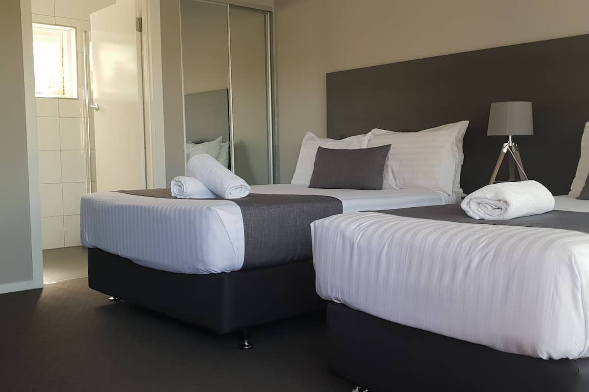 A hotel room with two beds, a mirror, a bedside lamp, and a view of the hallway.
