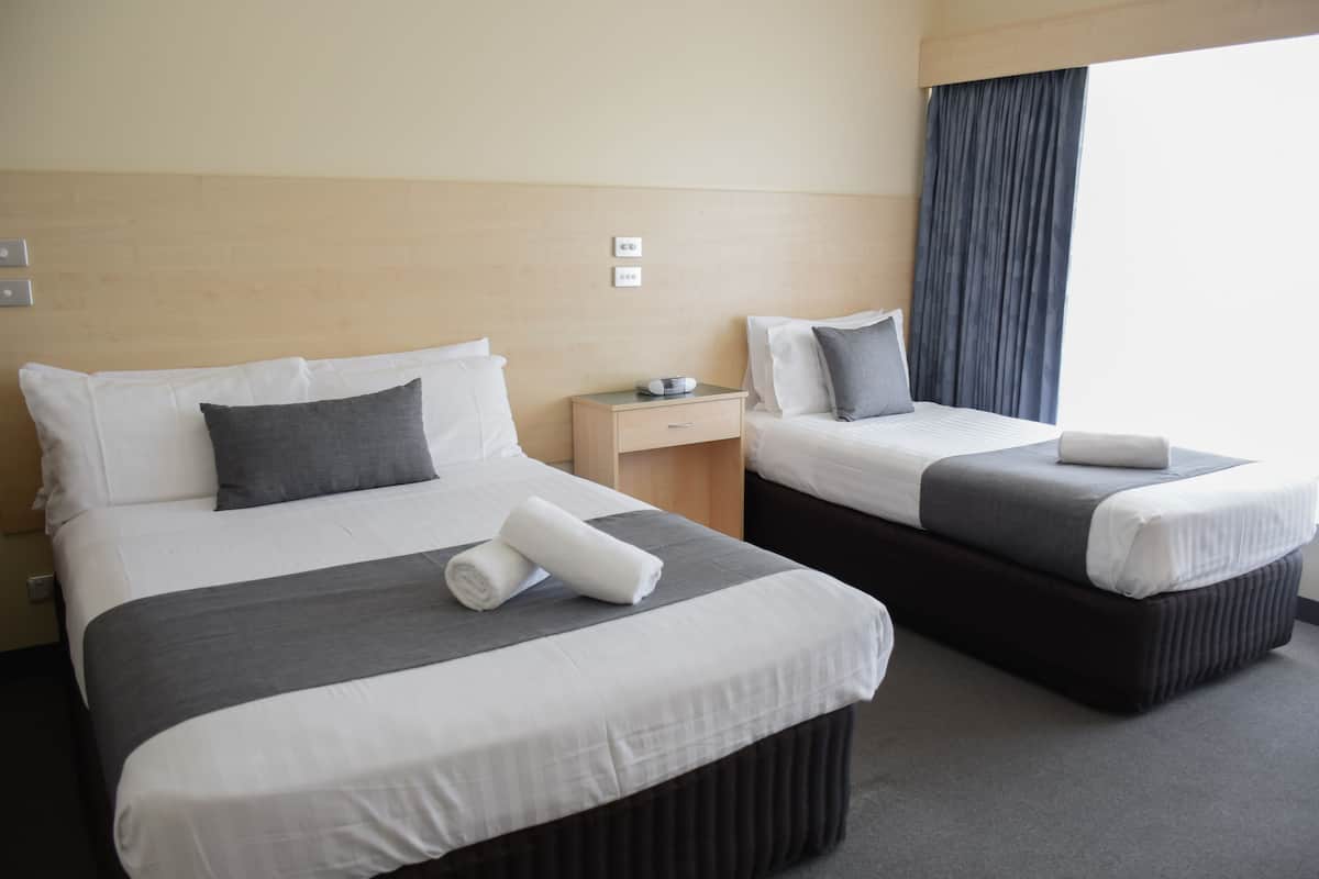 A hotel room with two beds, a nightstand, and a window with curtains.