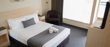 A hotel room with a bed, a chair, a desk, and a window.