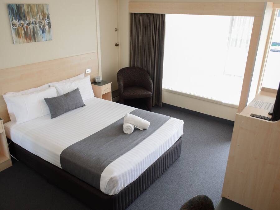 Una habitación de hotel con cama, una silla, un escritorio y una ventana.