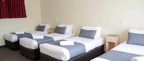 A hotel room with four single beds, each with a pillow and a blanket. There are bedside tables and a red curtain on the left wall.