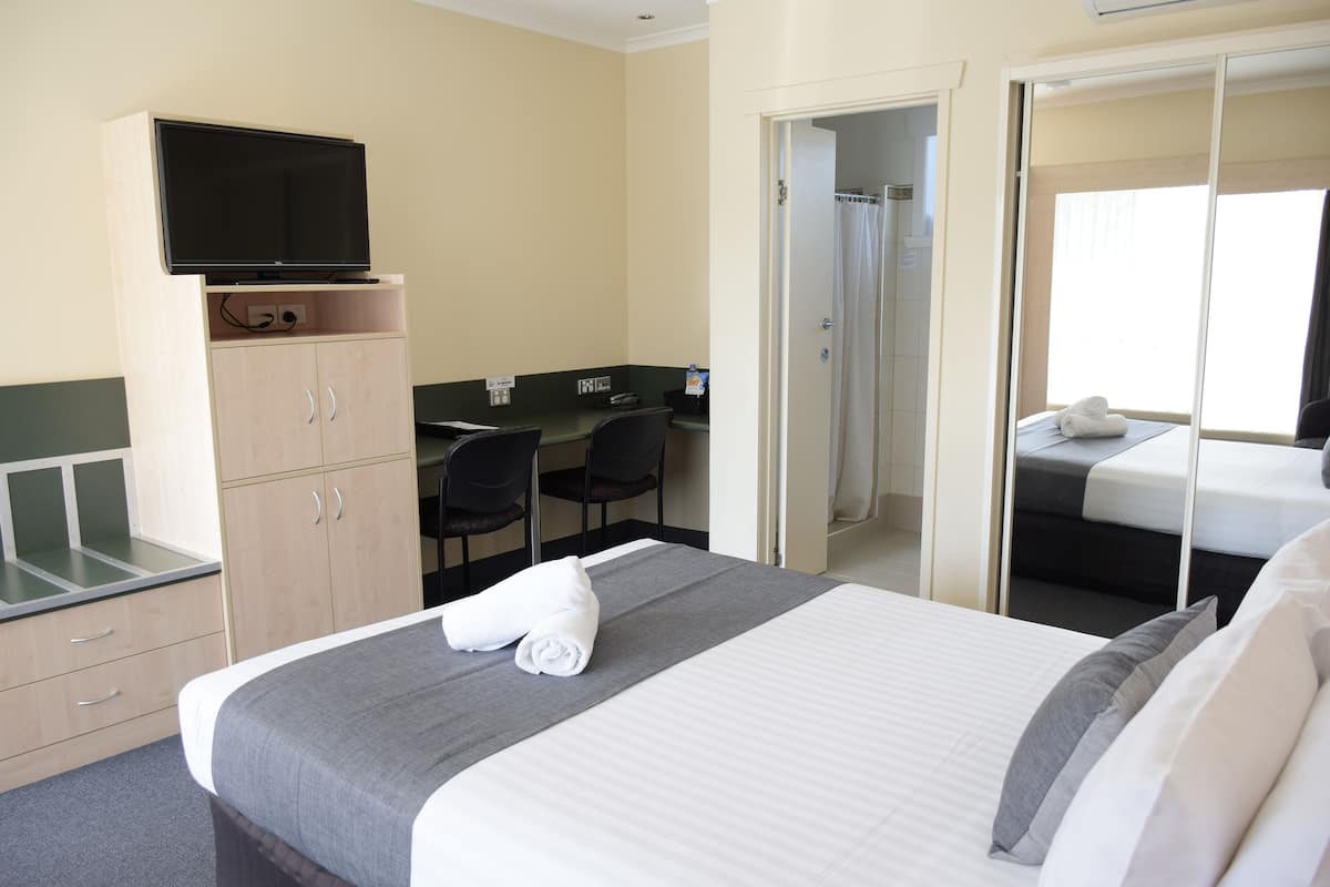 A hotel room with a bed, a desk, a television, a shower, and a wardrobe.