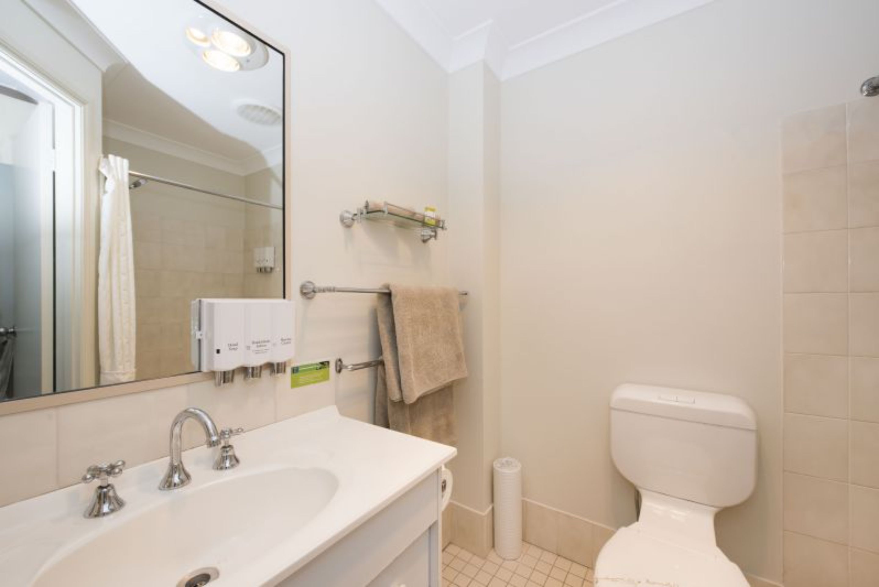Une salle de bain avec un lavabo blanc, un miroir, un porte-serviettes et des toilettes.