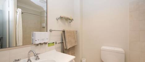 Une salle de bain avec un lavabo blanc, un miroir, un porte-serviettes et des toilettes.