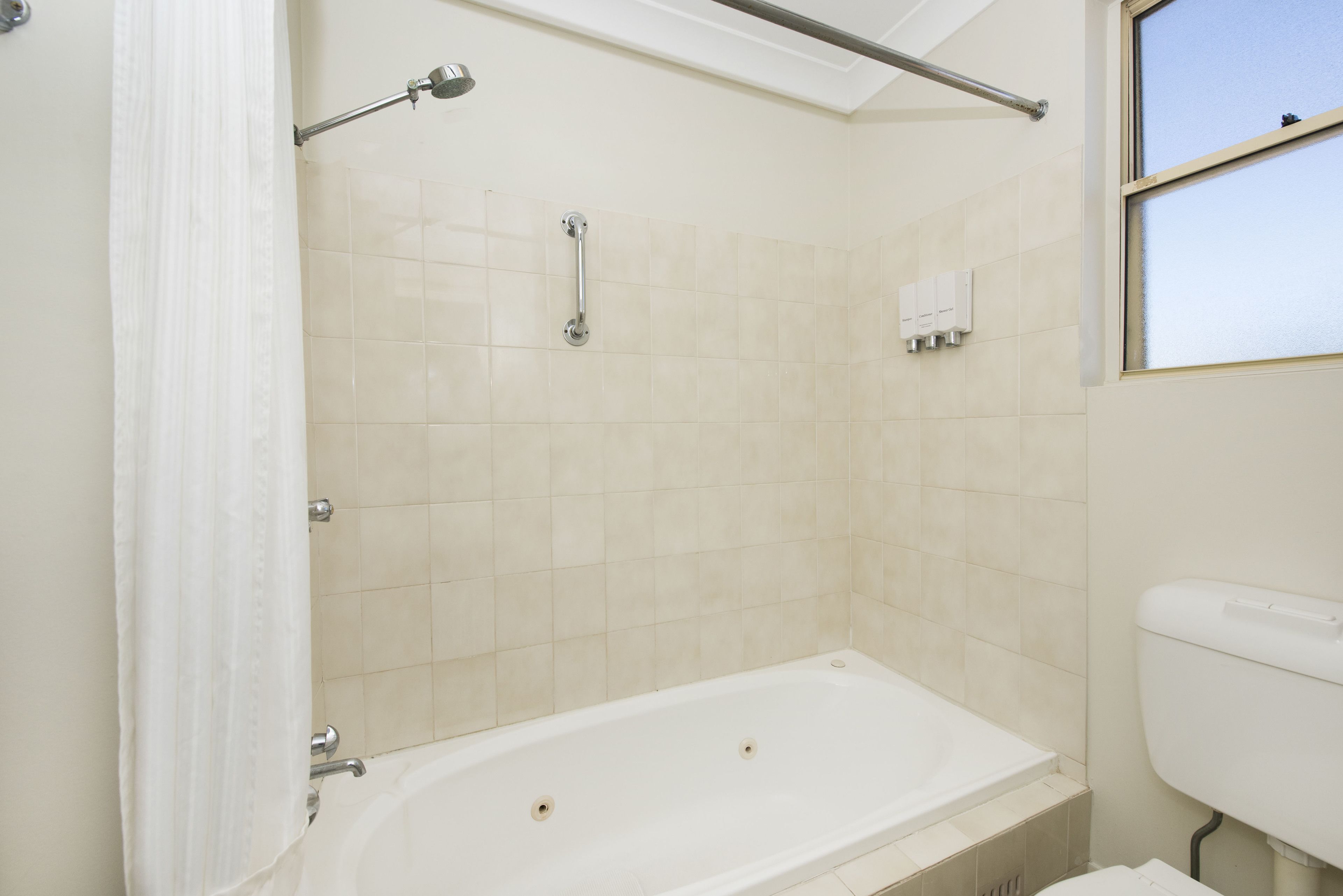 Un baño con bañera, cortina de ducha, barra de apoyo y retrete.