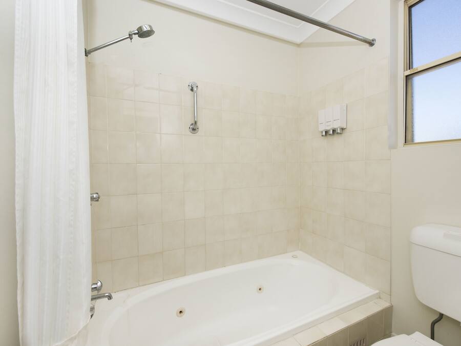 Un baño con bañera, cortina de ducha, barra de apoyo y retrete.