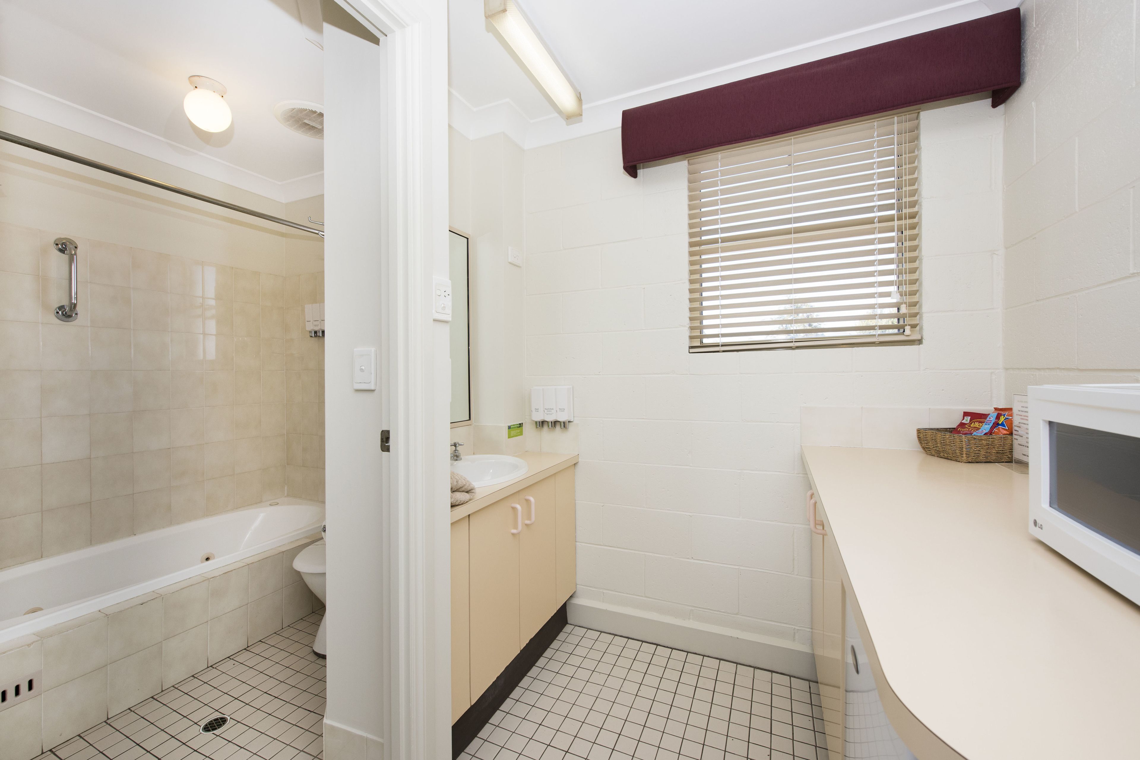 A bathroom with a bathtub, toilet, sink, and a window with blinds.