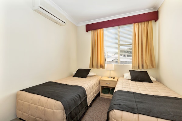 Une chambre d’hôtel avec deux lits, une fenêtre avec des rideaux, une table de chevet avec une lampe et un appareil de climatisation.