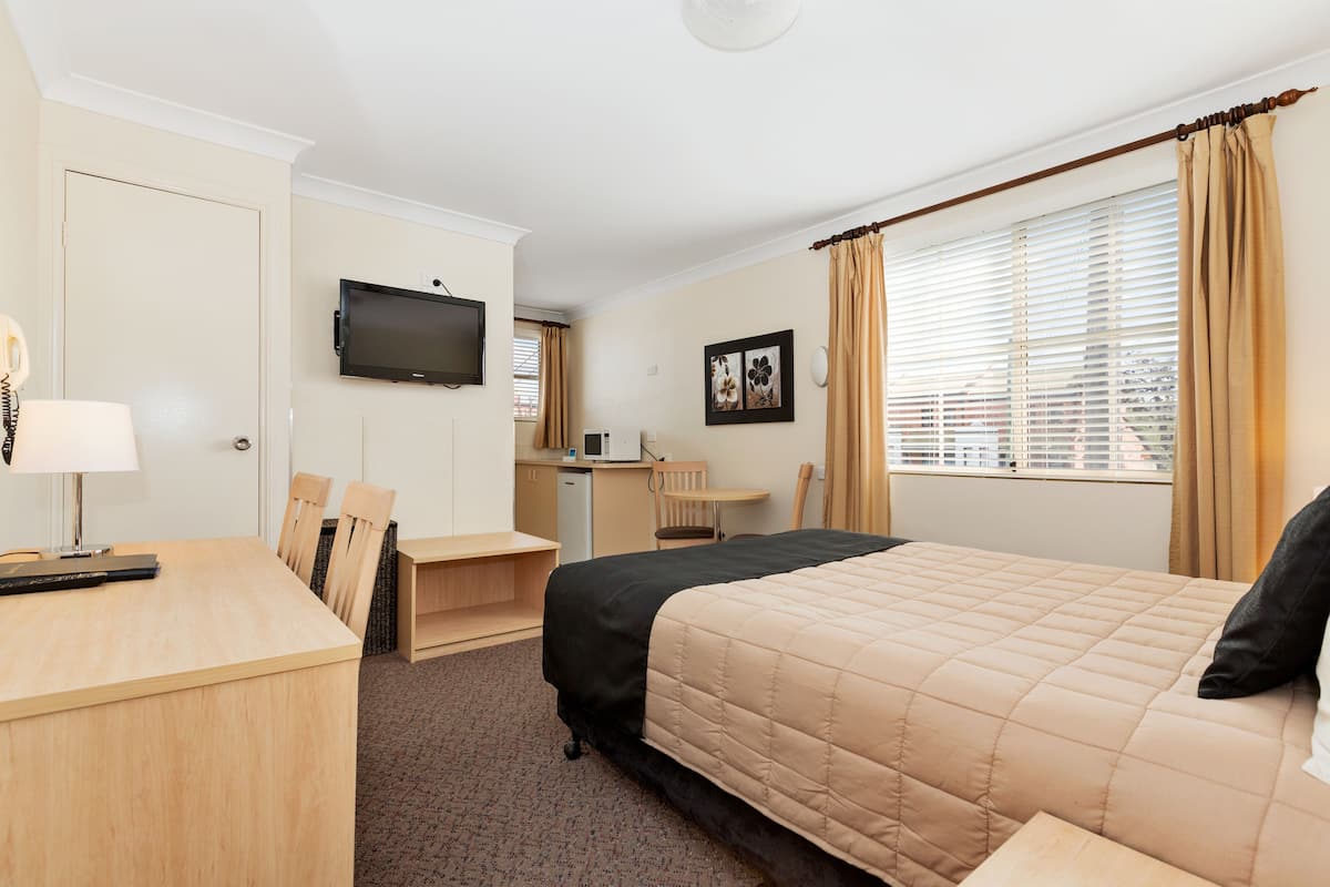 A hotel room with a bed, desk, chair, television, and a window with curtains.