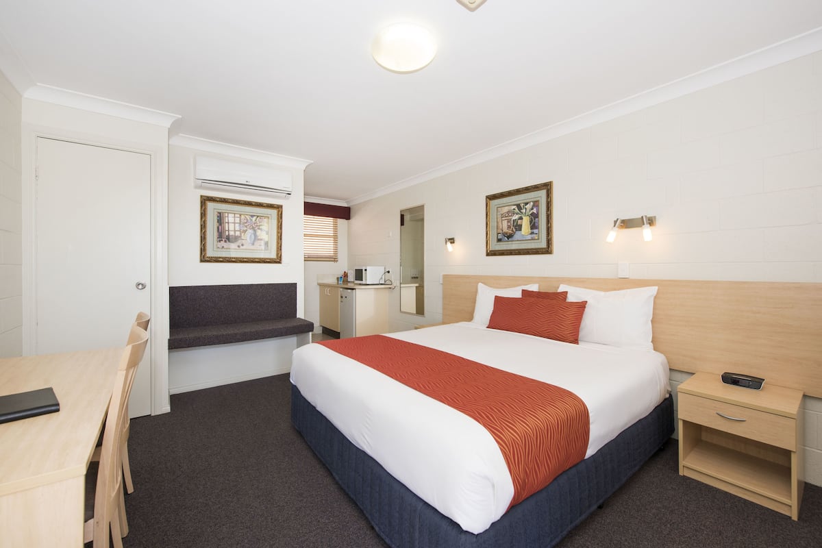 A hotel room with a large bed, bedside tables, a desk, and a chair. There are framed pictures on the walls and a ceiling light.