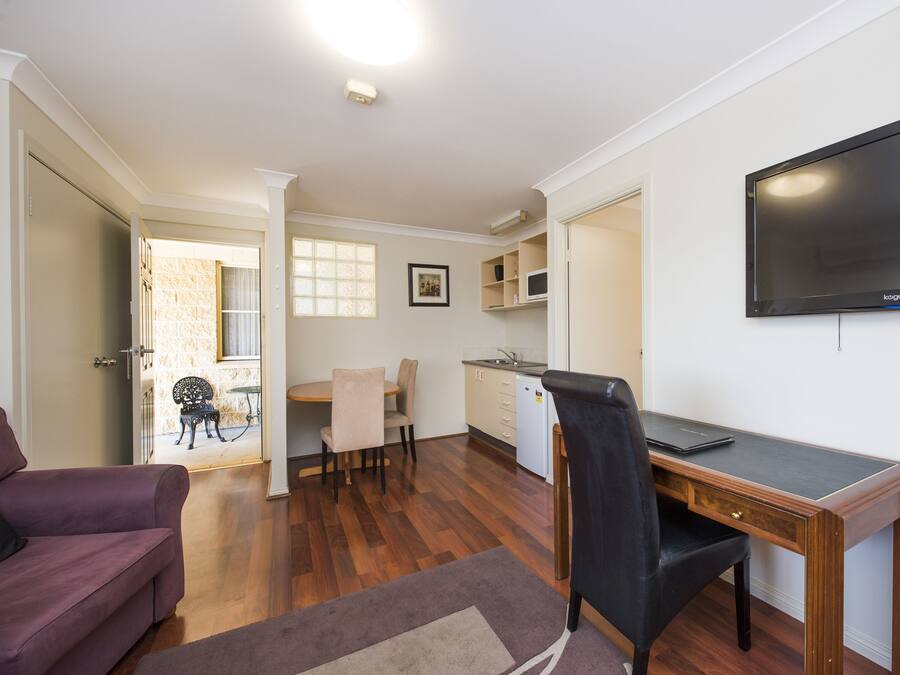 A compact living space with a kitchenette, a dining area, a sofa, and a TV mounted on the wall.
