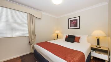 A hotel room with a large bed, two bedside lamps, a framed picture on the wall, and a window with curtains.