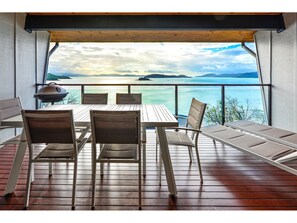 Une terrasse en bois avec une table et des chaises, donnant sur une étendue d’eau où l’on aperçoit des îles au loin.