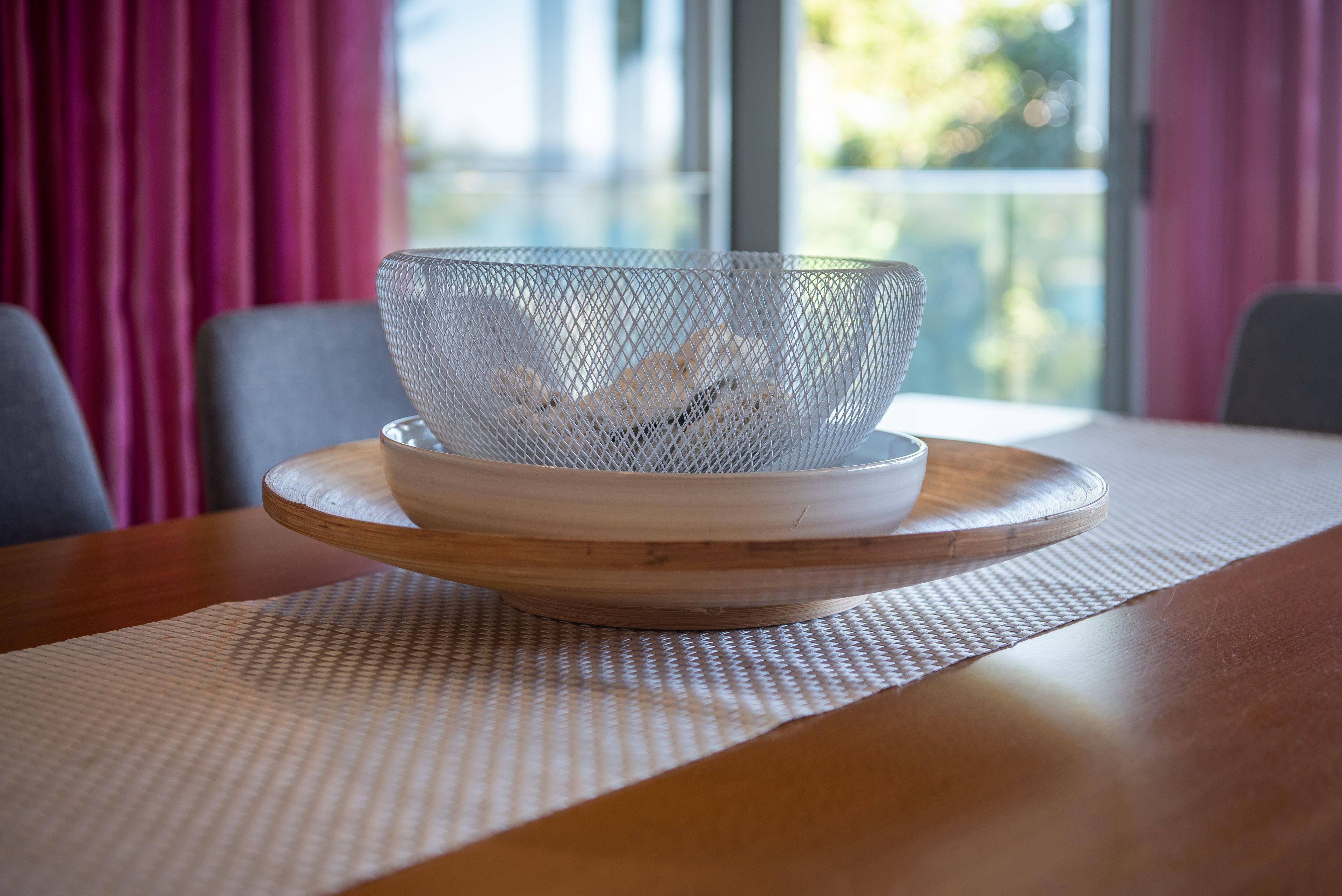 Een witte netkom op een houten dienblad, geplaatst op een tafel met een geweven placemat.