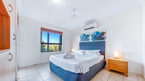 Un dormitorio con cama, mesita de noche y ventana.