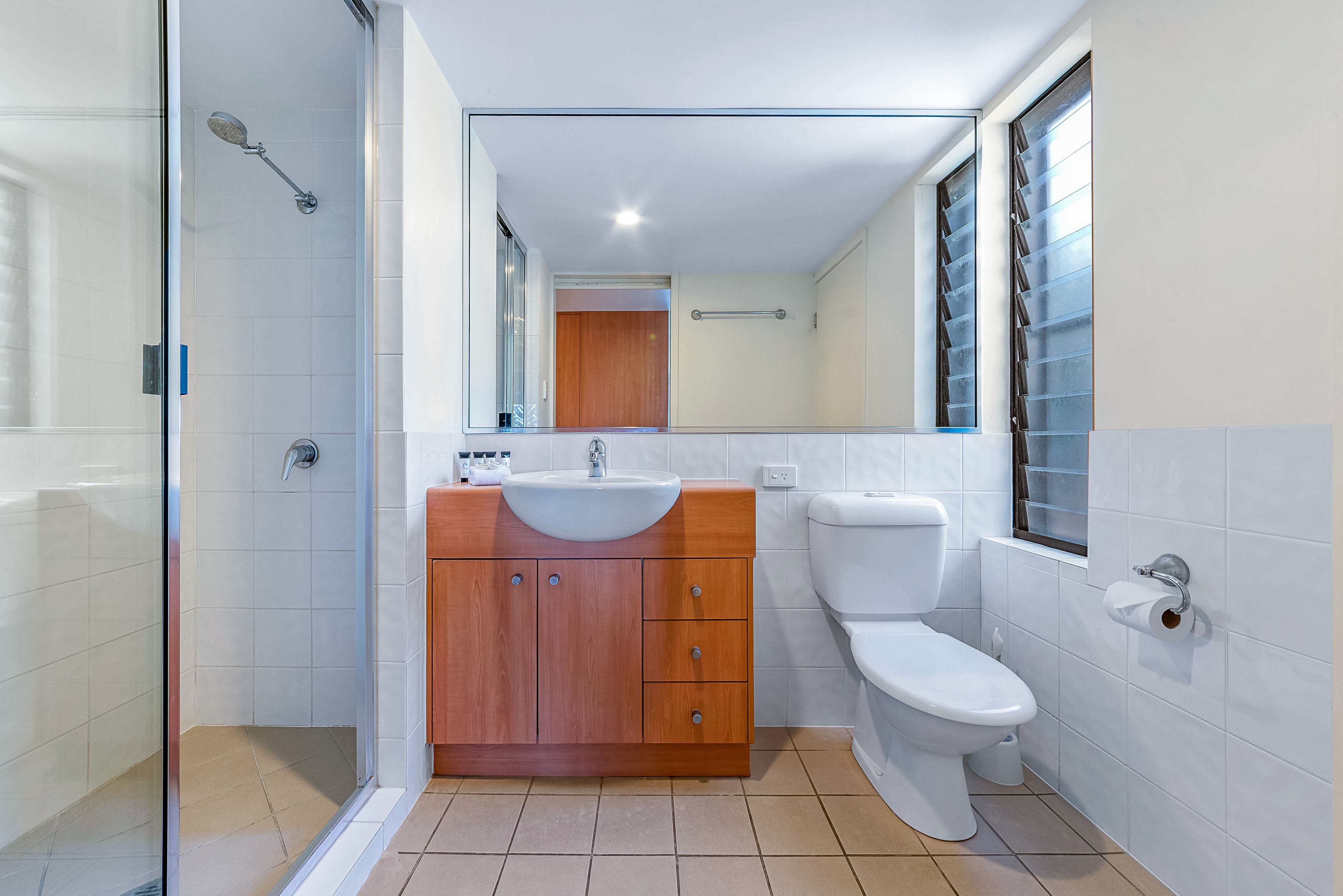 A modern bathroom with a glass shower enclosure, a wooden vanity with a sink, and a toilet.