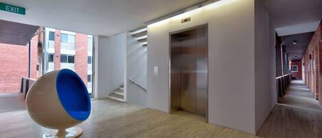A modern hallway with a unique blue and white spherical chair, an elevator, and a staircase.