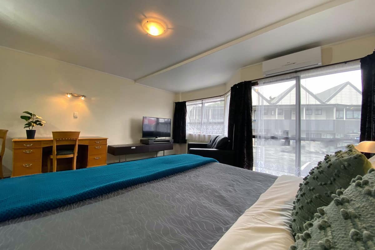 Ein Hotelzimmer mit Bett, Schreibtisch, Stuhl, Fernseher und großen Fenstern.