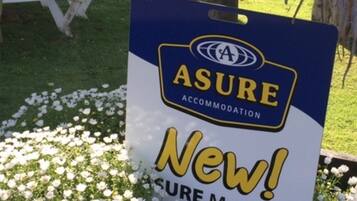 A sign for ASURE ACCOMMODATION with a "New! Sure Member" label, placed in front of a flower bed.