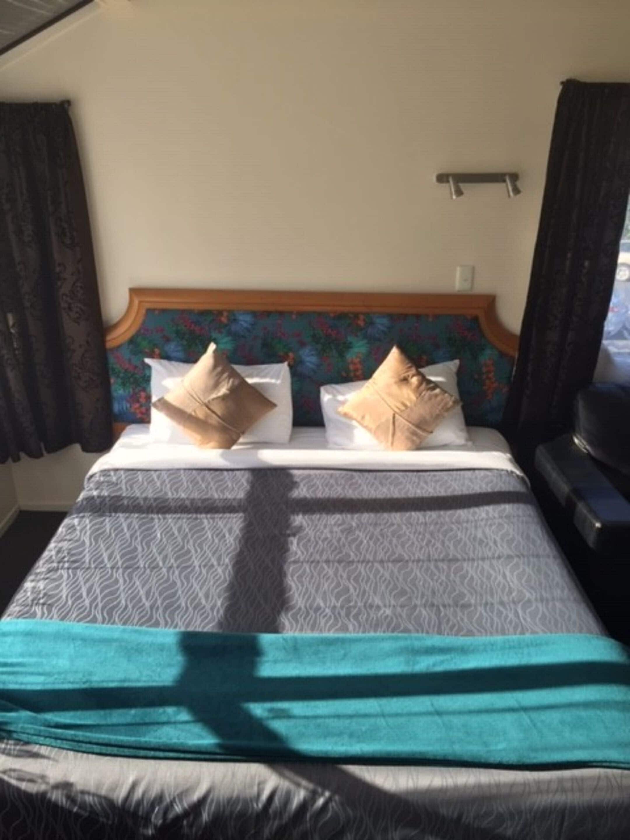 A bed with a patterned bedspread, two pillows, and a headboard with a floral design.