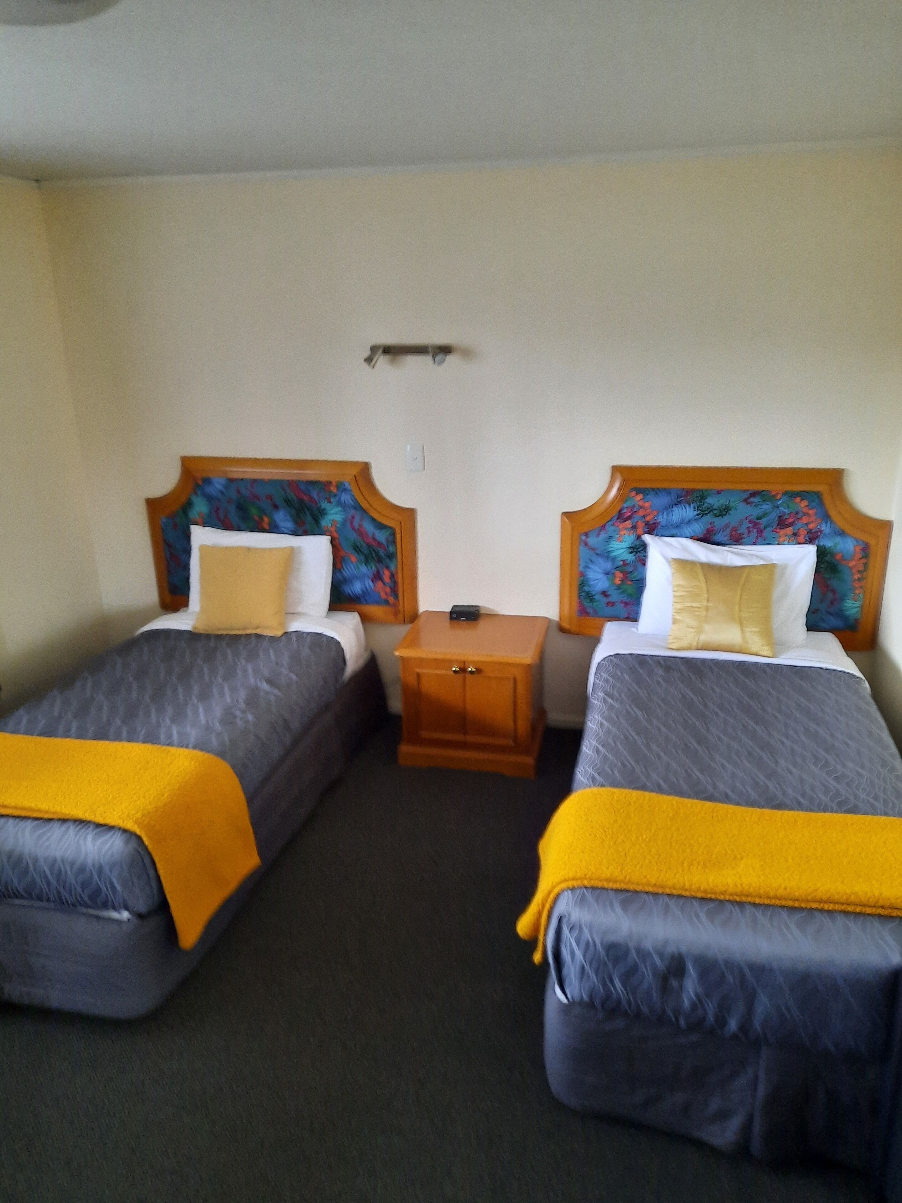 A hotel room with two single beds, each with a headboard, a nightstand, and a small table.