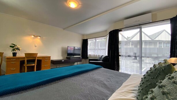 Habitación de hotel con cama, escritorio, silla, televisor y una ventana grande con vistas a edificios.