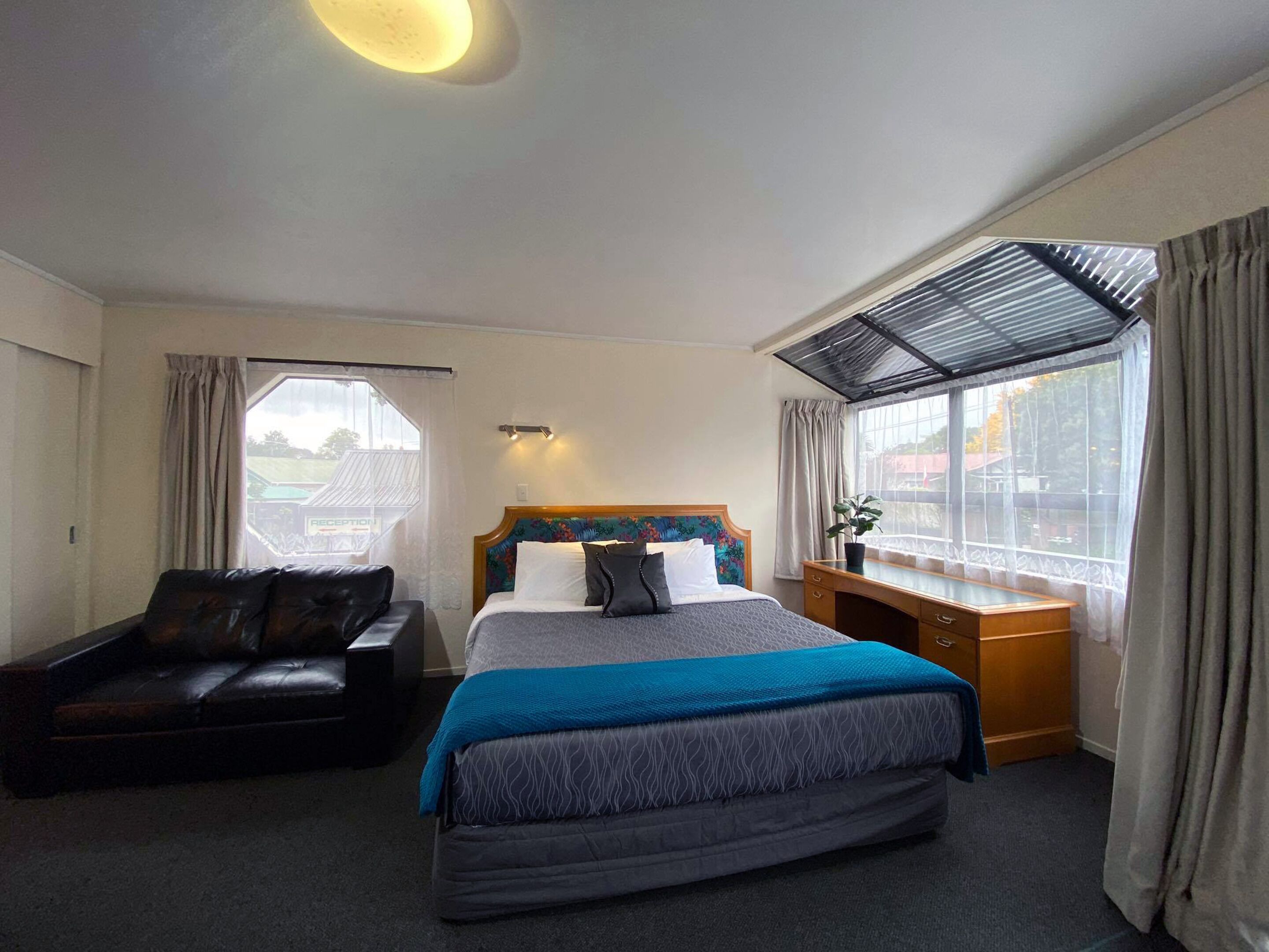 Quarto de hotel com cama, escrivaninha, cadeira e janela com cortinas.