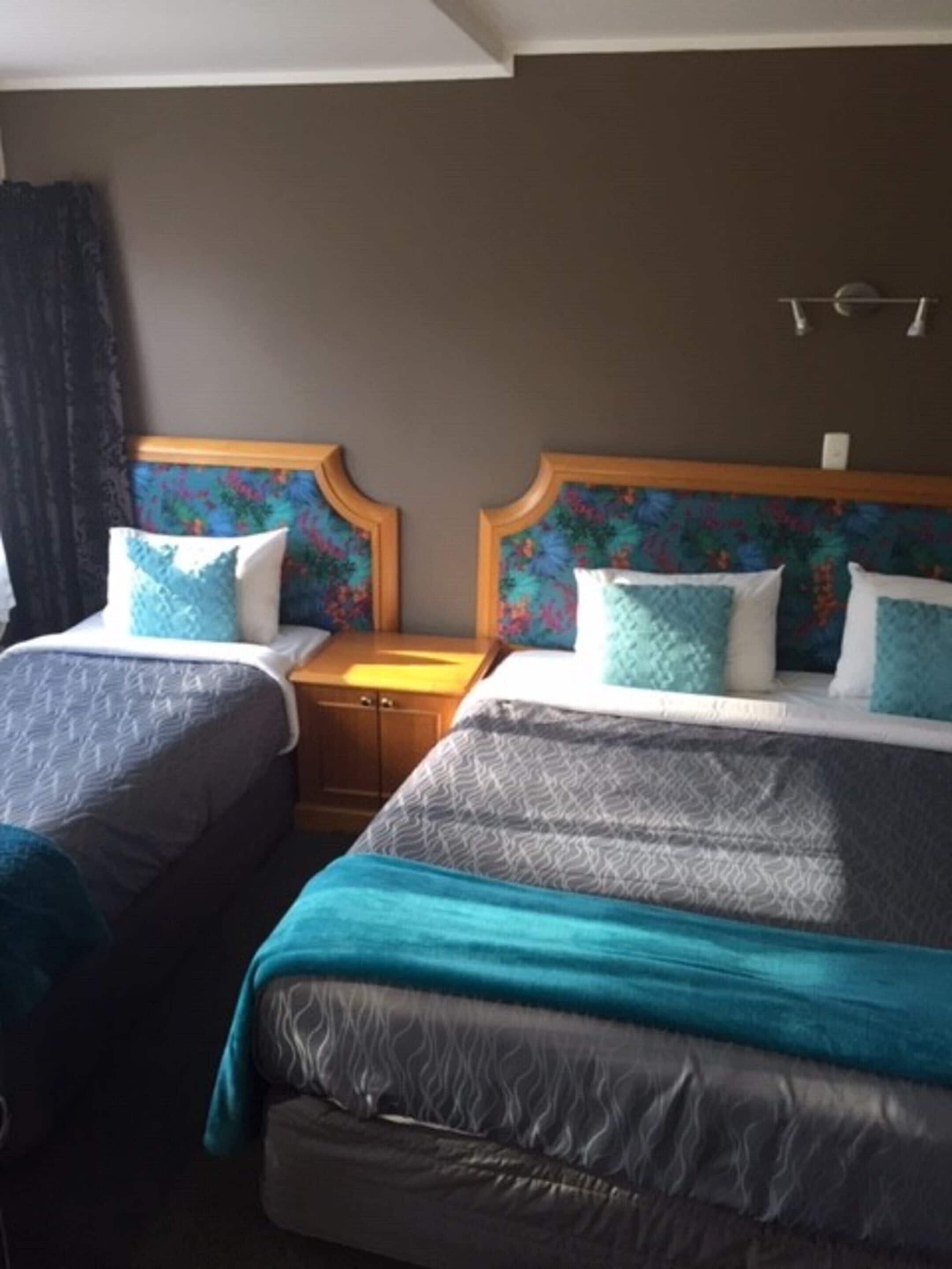 Een hotelkamer met twee bedden, elk met hoofdbord, een houten nachtkastje en een wandlamp.